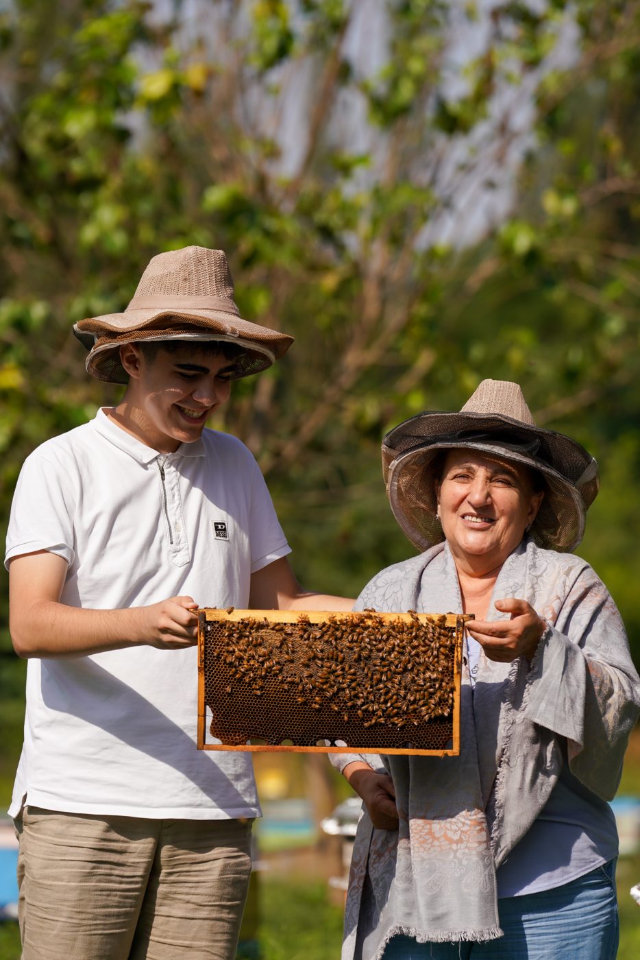 Two beekeepers smile while holding a honey frame together